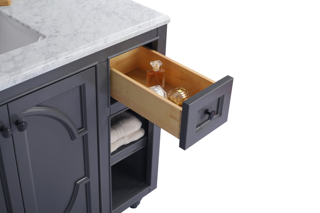 Gray bathroom vanity with marble countertop, open drawer, and towels.