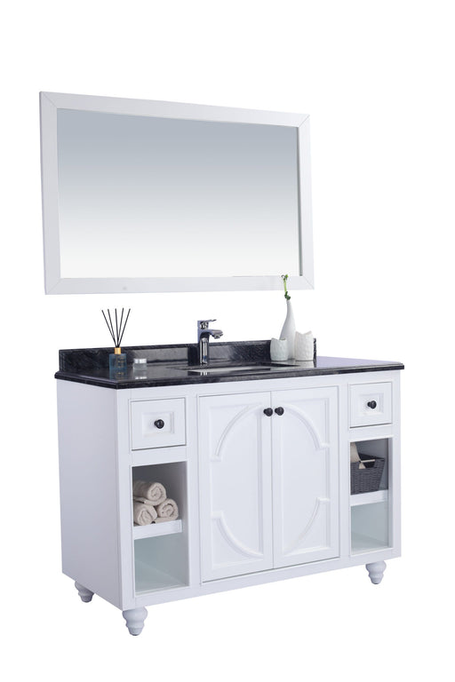 White bathroom vanity with black marble countertop, framed mirror, towels, and decor.