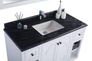 Close-up of a white bathroom vanity with a black marble countertop, a white sink, and a chrome faucet, accessorized with a diffuser, a small jar, and two decorative white vases.