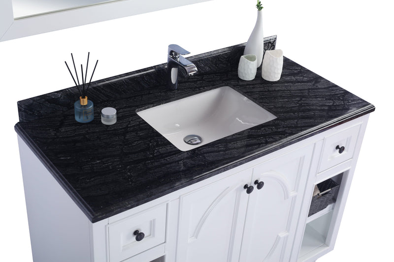 Close-up of a white bathroom vanity with a black marble countertop, a white sink, and a chrome faucet, accessorized with a diffuser, a small jar, and two decorative white vases.