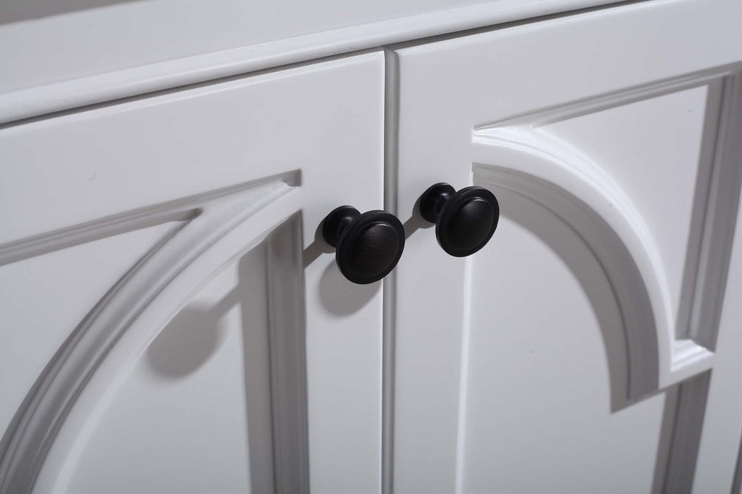Close up of a white cabinet with decorative arched molding and black knob pulls.