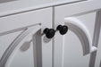 Close up of a white cabinet with decorative arched molding and black knob pulls.