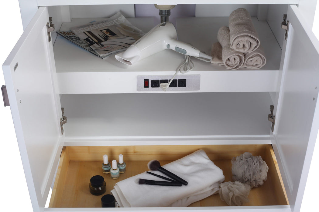 Bathroom vanity with white doors open revealing contents: magazine, hairdryer, rolled towels on a shelf, and a drawer with bottles, makeup brushes, and sponges.