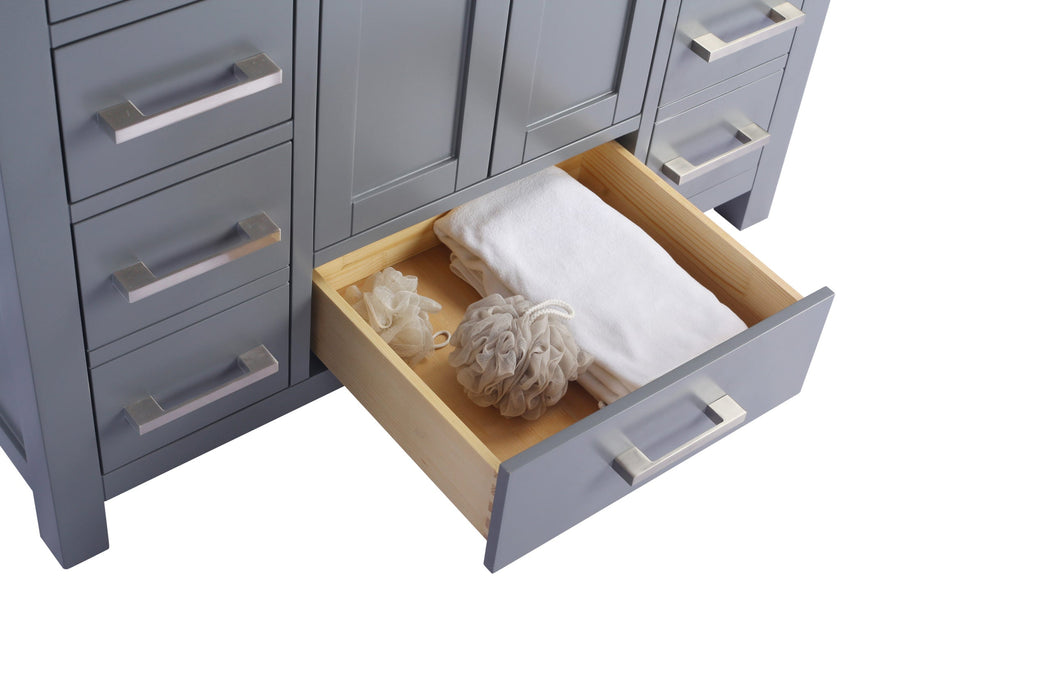 Gray vanity cabinet with open drawer revealing white towels and bath sponges.