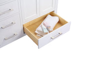 A white vanity cabinet with an open drawer containing a white towel and perfume boxes.