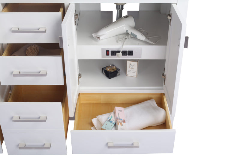 White vanity with open drawers and doors revealing a hair dryer, outlets, and toiletries.