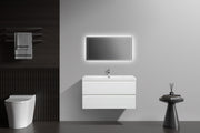 Modern bathroom with white floating vanity, LED mirror, toilet, towel rack, and decorative side table.
