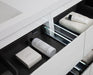 Open bathroom drawer with black interior, white towels and beauty products.