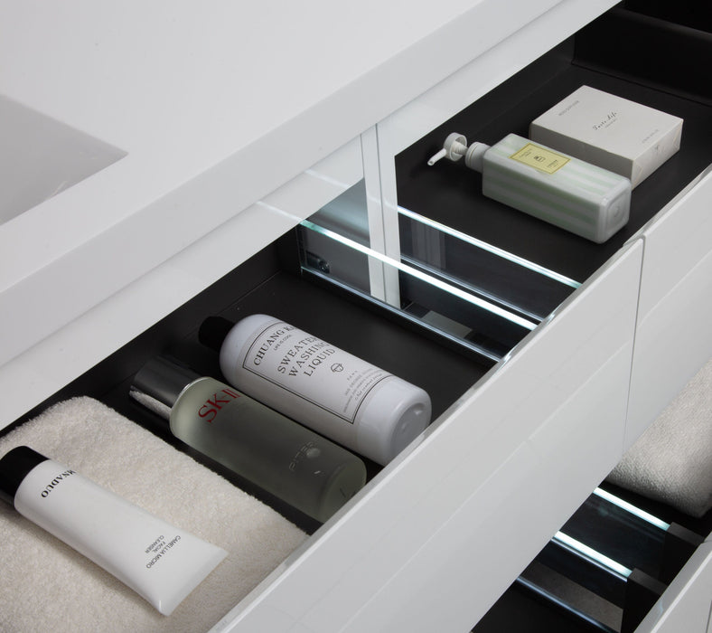 An open, illuminated drawer of a white bathroom vanity filled with skincare and cleaning products.