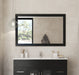 Bathroom vanity with a black cabinet, white countertop, and a black-framed mirror with a window.
