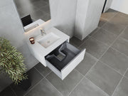 Bathroom vanity with open drawer, plant, candle, tiled floor and walls.