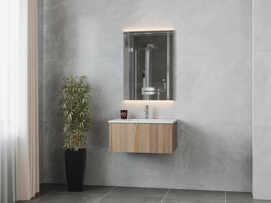 Modern bathroom vanity with wooden cabinet, white countertop, illuminated mirror, potted plant, and gray tile walls.
