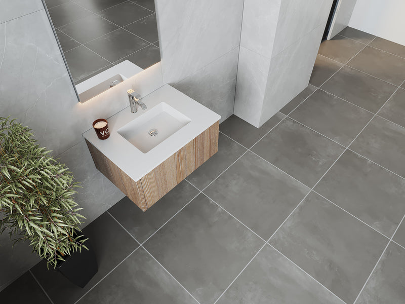 Modern bathroom featuring a wooden vanity with a white countertop sink, a silver faucet, a mirror, a potted plant, gray tile walls, and gray tile flooring.