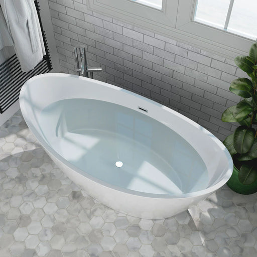 Modern white freestanding oval bathtub with blue-tinted water, set on hexagonal marble tiles with gray subway tile wall and green plant accent.