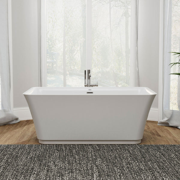 Modern white freestanding bathtub with chrome faucet, placed on a textured gray rug with hardwood floors and large windows in background.