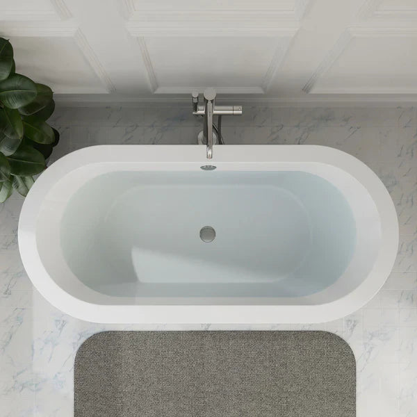 Modern white freestanding bathtub with chrome faucet, set on marble tiles with a green plant and gray bath mat.
