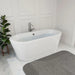 Modern white freestanding bathtub with sleek chrome faucet, placed on marble floor next to a green potted plant and gray bath mat.