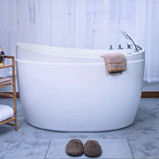Modern white freestanding bathtub with chrome fixtures, tan towel draped on edge, and brown slippers on bath mat in minimalist bathroom.