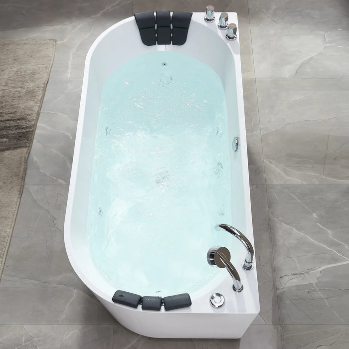 Modern white freestanding bathtub filled with light blue water, featuring black padded headrests and chrome fixtures on marble-like tiled floor.