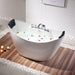 Modern white bathtub filled with water and flower petals, surrounded by wooden floor and white pebbles, with lit candles nearby.