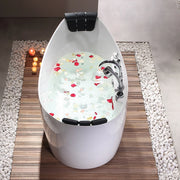 Modern white bathtub filled with water and scattered red and white rose petals, surrounded by lit candles on wooden deck and pebble tiles.