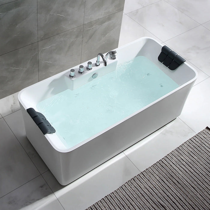 Modern white freestanding bathtub filled with light blue water, chrome faucet fixtures, and black headrests on marble-tiled bathroom floor
