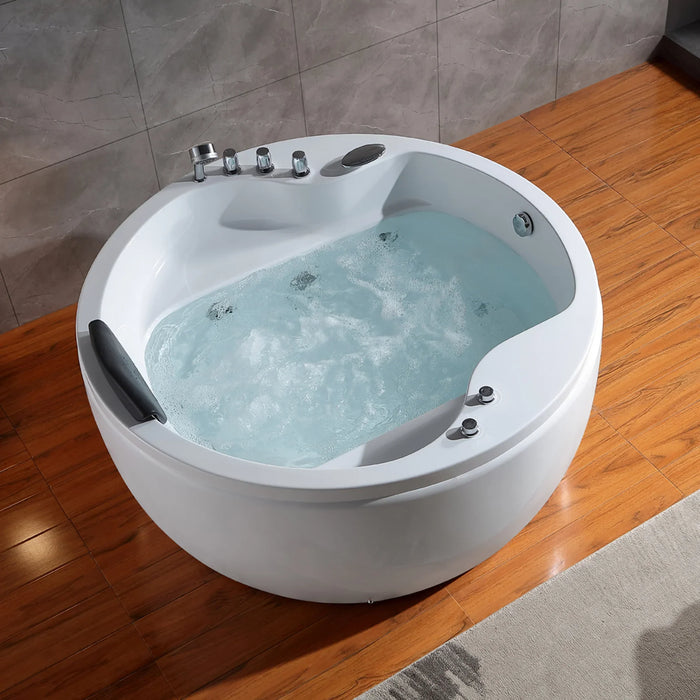 Round white whirlpool bathtub filled with bubbling blue-tinted water, set on wooden floor with gray tile wall background.