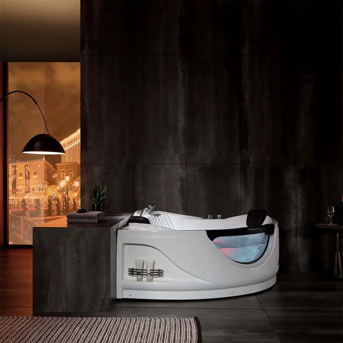 Modern white jacuzzi tub with curved glass panel, set against dark stone wall with warm city scene poster in background.