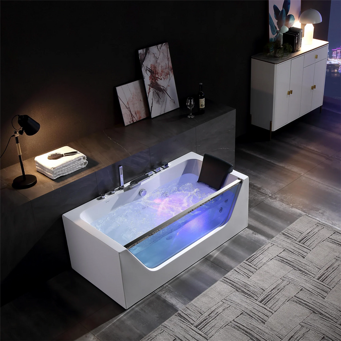 Modern white bathtub with blue and purple mood lighting, filled with bubbling water, placed in a dimly lit room with art and a desk lamp.