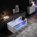 Modern white bathtub with blue and purple mood lighting, filled with bubbling water, placed in a dimly lit room with art and a desk lamp.
