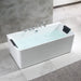 Modern white freestanding bathtub with water, chrome fixtures, and black headrest pillows, set against gray marble tiled wall.