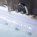 Sleek chrome bathtub faucets and handheld showerhead, with flowing water creating rippling white and blue reflections.