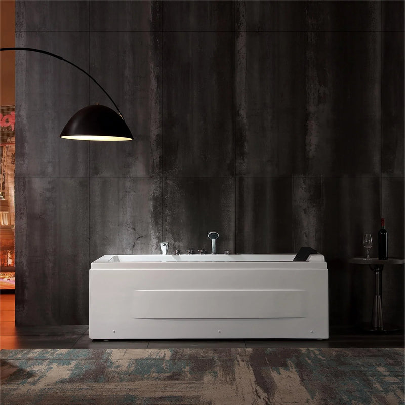 White rectangular bathtub against dark concrete wall, illuminated by arched black floor lamp, with wine glass and bottle nearby.