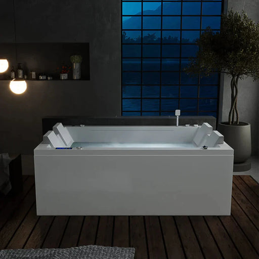 Modern white bathtub with geometric headrests, placed on wooden floor with large blue-tinted window revealing mountain silhouette at night.