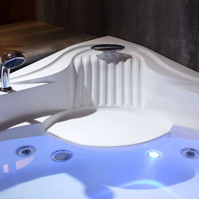 White jacuzzi tub with curved design, blue-lit water, and chrome shower head against dark textured wall.