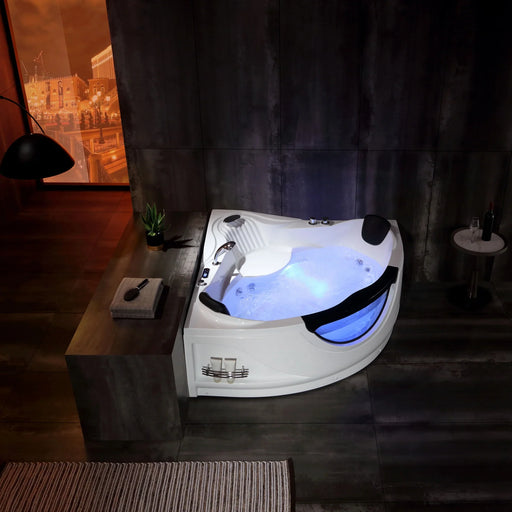 Modern corner bathtub with blue underwater lighting, surrounded by dark tiled bathroom with warm orange cityscape view through window.