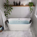Modern white bathtub filled with blue water, surrounded by white subway tiles, hanging plants, and a wooden shelf with candle and dark bottles.