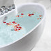 White bathtub filled with pale blue water and scattered red and pink rose petals, chrome faucet visible on left side.