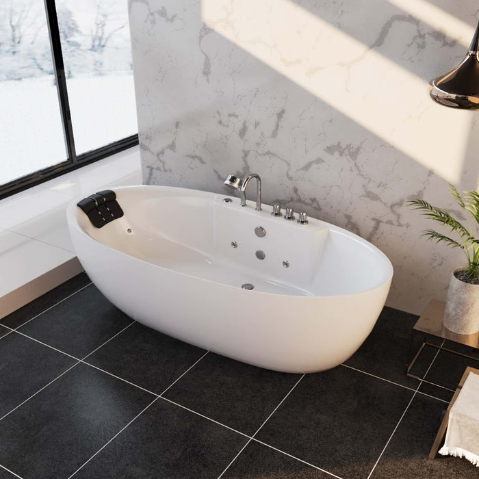 Modern white freestanding bathtub with jets, placed on dark tiled floor near large window with snowy landscape outside, marble wall backdrop and small potted plant.