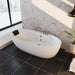 Modern white freestanding bathtub with jets, placed on dark tiled floor near large window with snowy landscape outside, marble wall backdrop and small potted plant.