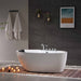 Modern bathroom with white freestanding tub, lit candles, wooden mat, and landscape artwork on dark tiled wall.