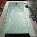 High-tech bathtub filled with turbulent water, illuminated with green lights and featuring multiple water jets and a digital control panel.