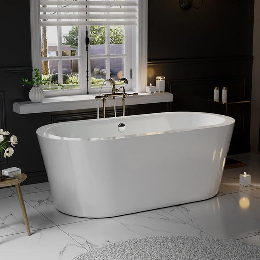 Modern white freestanding bathtub with brass fixtures, placed on marble floor near window with garden view and candles.