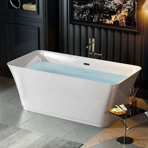 Modern white freestanding bathtub filled with light blue water, placed on gray tile floor with side table and diffuser.