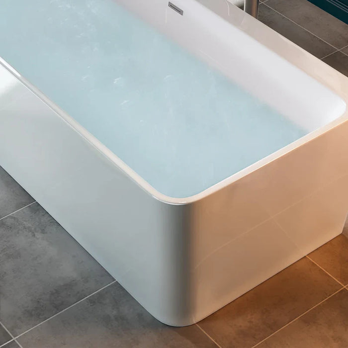 Modern freestanding bathtub filled with light blue water, white sides, sitting on tiled bathroom floor with warm and gray tones.