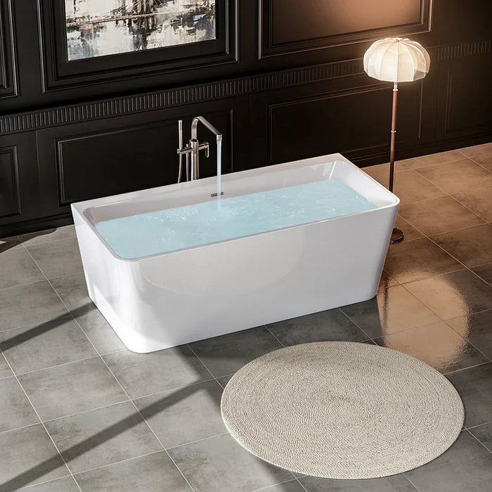 Modern white freestanding bathtub filled with blue water, beside a vintage floor lamp on dark tiled bathroom floor with round beige rug.