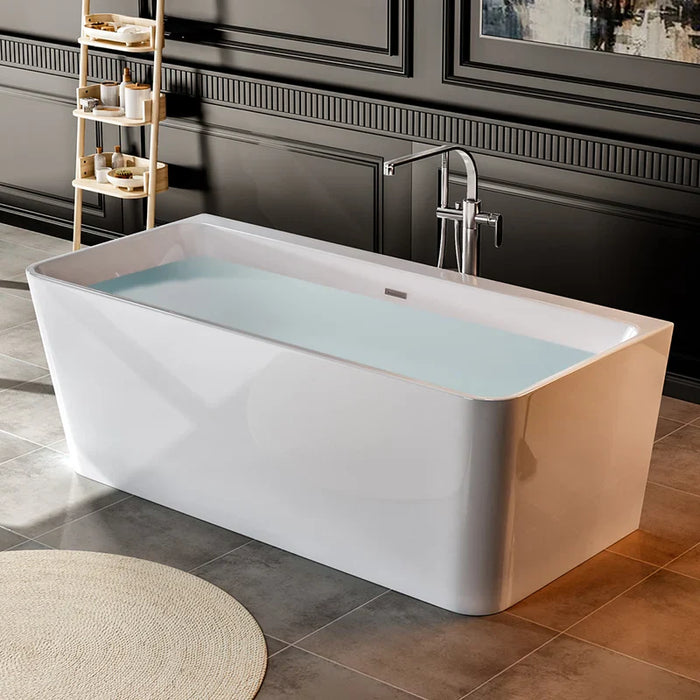 Modern white freestanding bathtub filled with pale blue water, positioned on tiled floor with decorative shelving unit and chrome faucet.