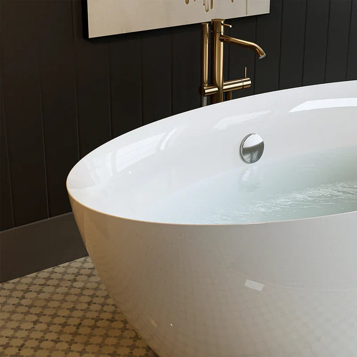 Glossy white freestanding bathtub with golden faucet, partially filled with water, against dark paneled bathroom wall with patterned tile floor.