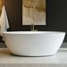 Modern white freestanding bathtub with gold faucet, set against dark paneled wall with abstract drip art featuring a bare tree.