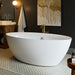 Modern white freestanding bathtub in elegant bathroom with dark walls, gold-toned wall art, and decorative mosaic floor tiles.